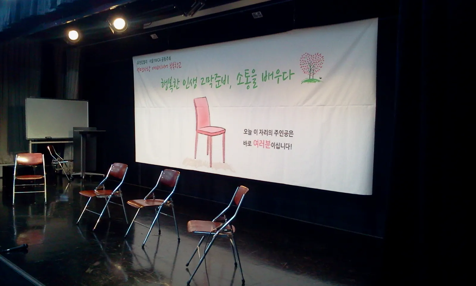 부부학교 심리극 무대. 하얀 현수막 앞에 빈 의자들이 놓여 있다